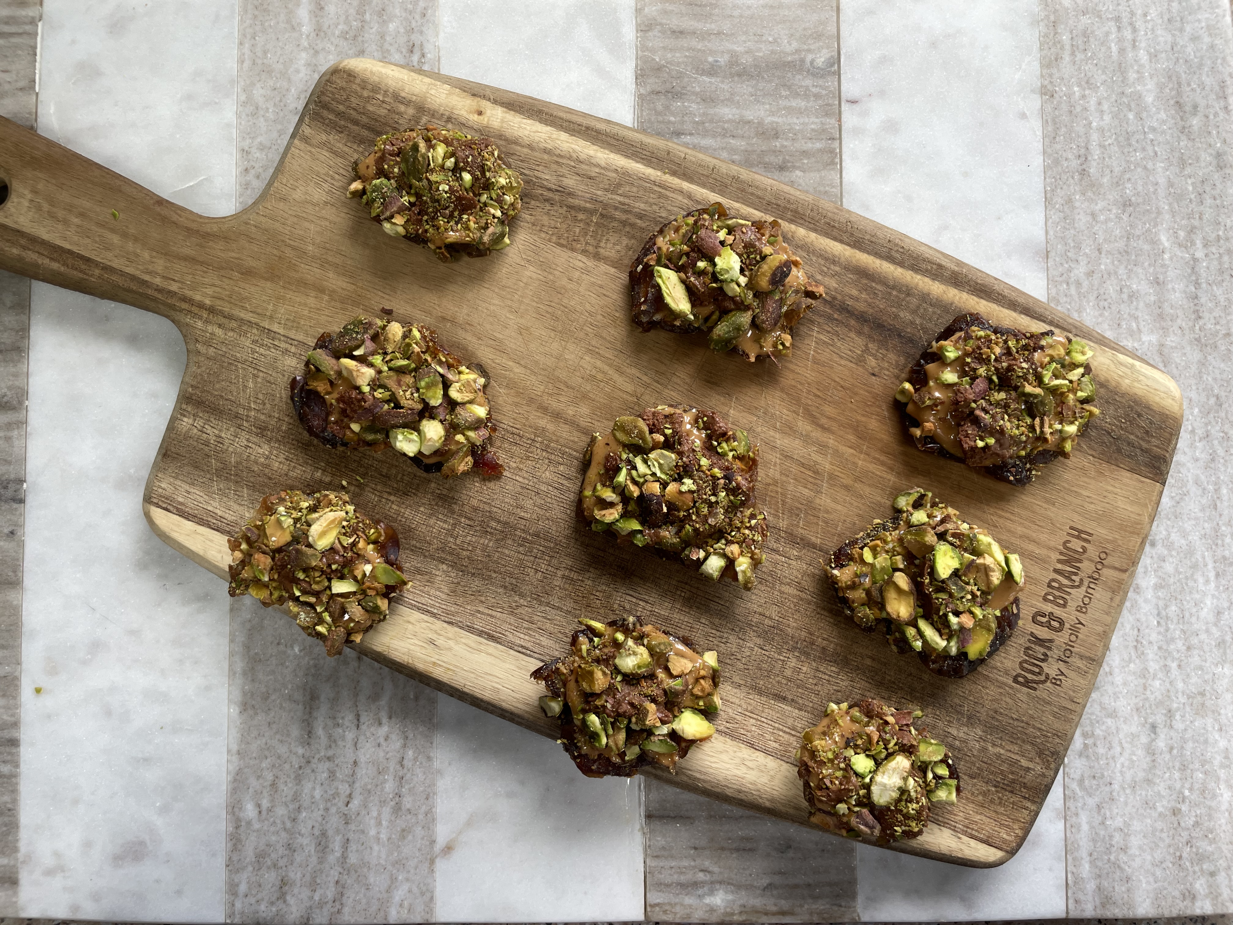 Viral date snacks topped with peanut butter, melted chocolate, and crushed pistachios on a wooden board
